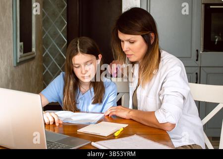 Mom and daughter surfing internet on laptop sitting in kitchen, online shopping. Watching something exciting on internet Stock Photo