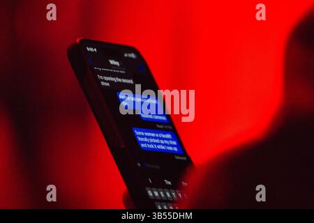 Close-up of a smartphone displaying a text message conversation against a stark red background. The screen shows blue text bubbles with a partially vi Stock Photo