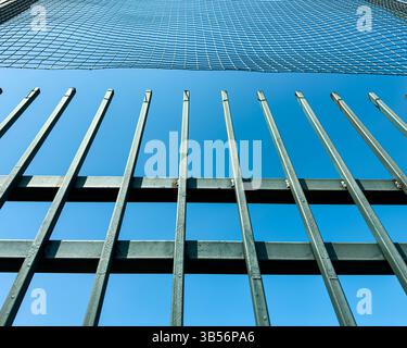 Metal fence with vertical bars and protective netting against clear blue sky. Urban detail, geometric structure, no people, abstract composition. Stock Photo