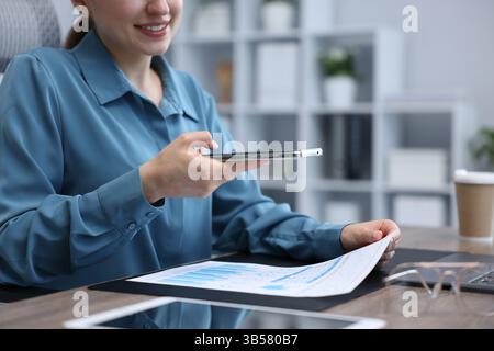 Woman taking photo of document using scanning app on smartphone at desk in office, closeup Stock Photo
