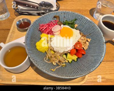 Colorful Asian-inspired rice bowl topped with a sunny side egg, vegetables, and ground meat served with tea and coffee, perfect for a healthy brunch Stock Photo