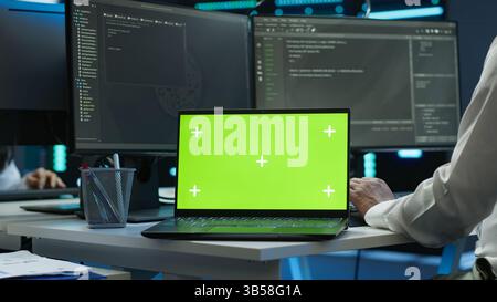 System administrator in data center installing software on isolated screen laptop, troubleshooting issues. Admin uses mockup notebook in server hub, establishing performance benchmarks, camera A Stock Photo