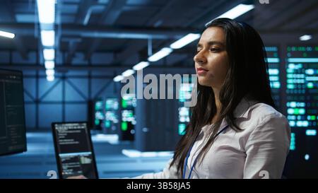 Computer scientist in data center monitoring security threats using PC, implementing cybersecurity measures. Server farm employee ensuring compliance with regulations, camera B Stock Photo