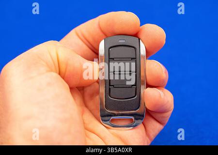 four-button remote control for opening garage doors held in hand on blue background Stock Photo