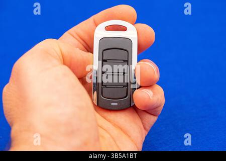 four-button remote control for opening garage doors held in hand on blue background Stock Photo