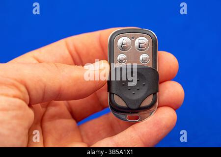 four-button remote control for opening garage doors held in hand on blue background Stock Photo
