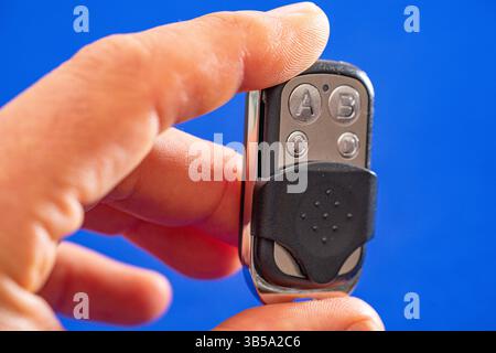 four-button remote control for opening garage doors held in hand on blue background Stock Photo
