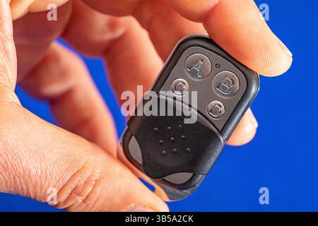 four-button remote control for opening garage doors held in hand on blue background Stock Photo