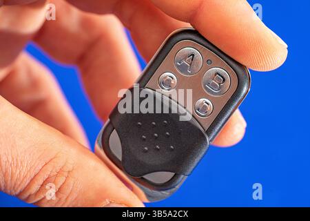 four-button remote control for opening garage doors held in hand on blue background Stock Photo