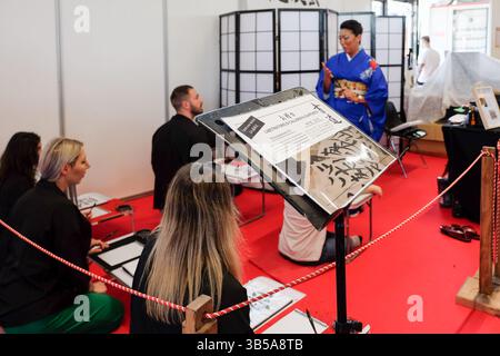 Milan, Italy. 1 May, 2025. Participants attend a Japanese calligraphy class led by an instructor in kimono at Festival dell'Oriente, in Novegro Park. Stock Photo
