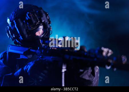 Special forces soldier wearing tactical gear and night vision goggles preparing for a mission in low light. Stock Photo