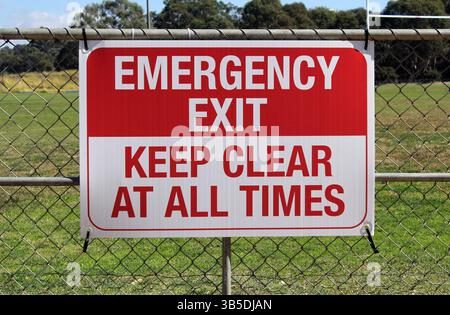 Red and white Emergency Exit sign attached to a fence Stock Photo