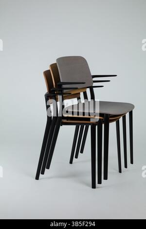 three modern wooden chairs with black metal frames are stacked neatly against a white background the composition highlights simplicity and contemporar Stock Photo