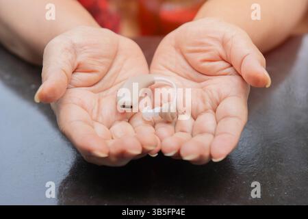 Person with disability, deaf and people, trust and communication, health insurance and medical. Hearing aid on elderly woman hands. Stock Photo