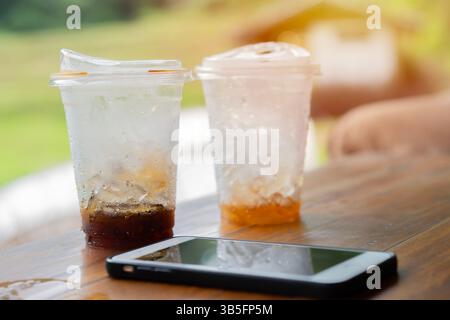 Close up ice cube in the glasses of coffee with phone on the wooden table after drink. Lifestyle concept. Selective focus. Stock Photo