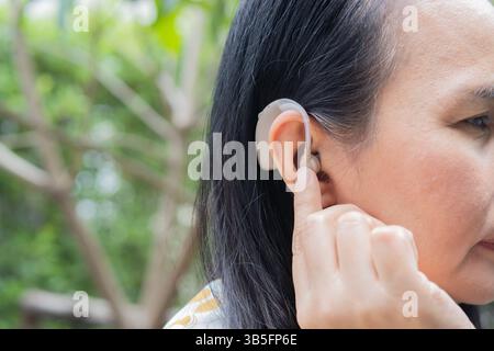 Hearing aid behind the ear of senior woman over nature background. Close-up, copy space. Side view. Stock Photo