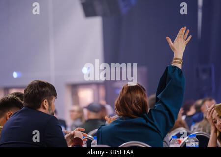 Group of conference participants interactively engaging in discussion with one raising hand actively. Stock Photo