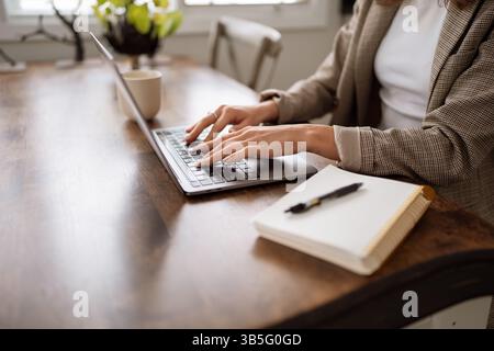 Person writing in notebook beside laptop on wooden desk. Stock Photo