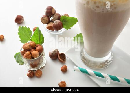 Hazelnut smoothie with bowls of fruit and leaves and glass filled with cream drink on a white plate with straw. Top elevated view. Stock Photo