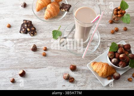 Refreshing hazelnut drinks in glass cup and croissants on wooden table with nuts. Top view. Stock Photo