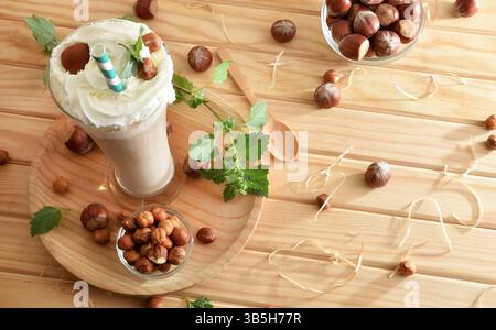 Background with freshly made hazelnut drink with cream on a wooden table with hazelnuts around. Top elevated view. Stock Photo