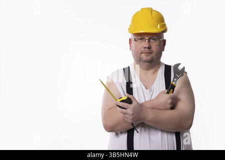 A construction worker wearing a yellow hard hat is holding tools and is prepared for various construction tasks ahead Stock Photo