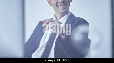 Close up crop portrait shot of a smiling and confident young businessman in black suit at office Stock Photo