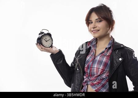 A trendy young woman confidently poses with an alarm clock, showcasing her stylish outfit and vibrant demeanor Stock Photo
