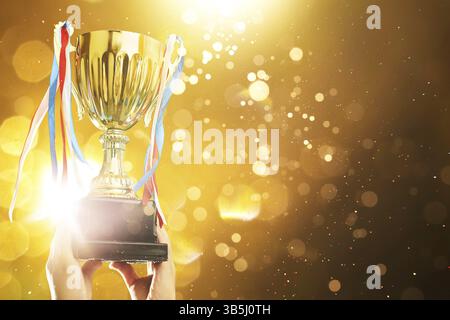 Hand raised, holding gold cup with abstract shiny lights . award and victory concept Stock Photo