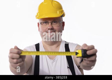 A construction worker in a yellow hard hat measures using a tape measure, showcasing tools of the trade Stock Photo