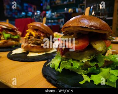 Three different gourmet burgers, each with unique toppings including meat, cheese, bacon, pulled pork, tomatoes, and pickles, are presented on black s Stock Photo