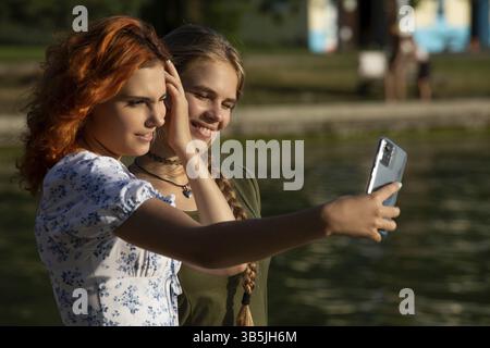 Two young women are joyfully taking a selfie by the water, capturing a beautiful moment of genuine friendship Stock Photo
