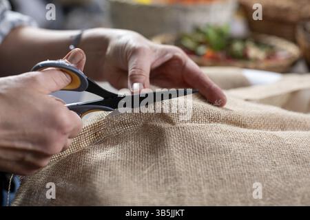 A detailed closeup view of hands skillfully using scissors to neatly cut burlap fabric for various crafting projects Stock Photo