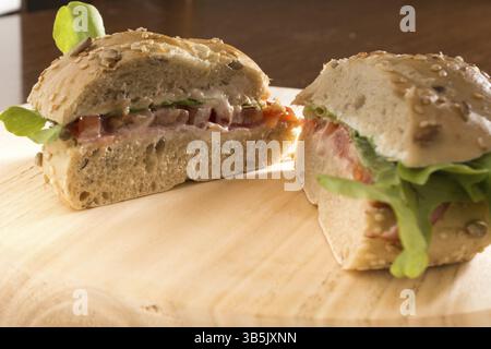 Sandwich with fresh smoked meat, cheese, lettuce and tomato with homemade ketchup sliced in half Stock Photo