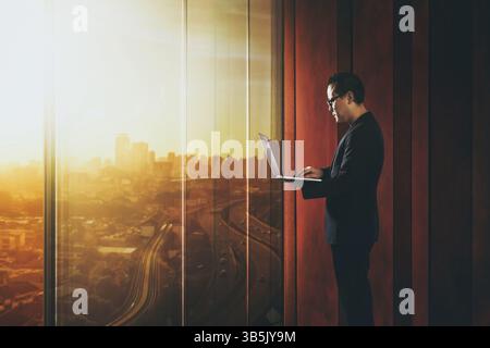 Businessman using laptop with generic office background, night scene Stock Photo