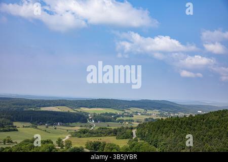 A stunningly beautiful view of rolling green hills stretching under a clear blue sky adorned with fluffy white clouds Stock Photo