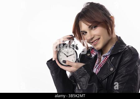 A stylish young woman smiles broadly while confidently holding an alarm clock, showing a joyful sense of urgency Stock Photo