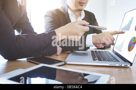Two businessmen discussing the charts and graphs showing the results of their successful project .Digital tablet, smart phone and laptop computer usin Stock Photo