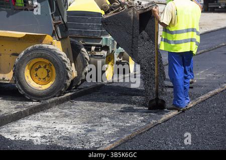 Team of workers put the hot asphalt on a street along tram car's railroad lines. Road construction workers with shovels in protective uniforms and an Stock Photo