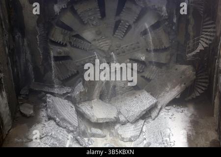Tunnel Boring Machine front head element is seen rotating on a subway station under construction. Dust and water Stock Photo