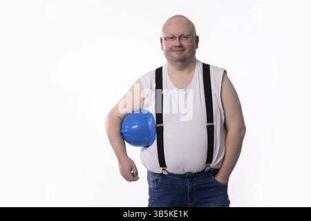 A confident construction worker in a sleeveless shirt and blue hard hat, standing with arms crossed Stock Photo