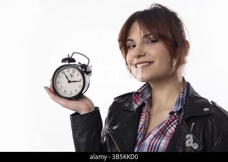 A cheerful young woman confidently poses with an alarm clock, showcasing her style and time management skills Stock Photo