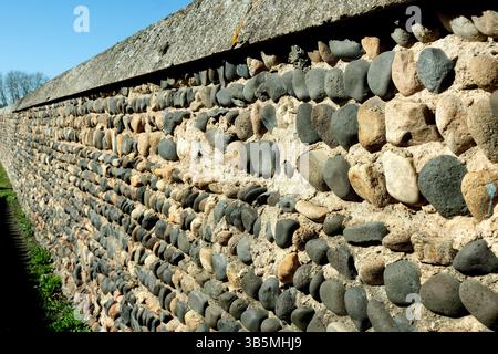 A close-up view of a stone wall constructed from various pebbles and cobbles creates an interesting texture against the clear blue sky. France Stock Photo