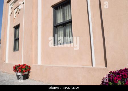 Mediterranean charm: Peach-colored building facade adorned with vibrant flowers in planters, featuring traditional barred windows Stock Photo
