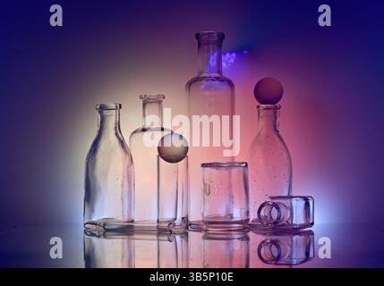Old vintage glass bottles and jar on a reflective surface and colorful back lighting Stock Photo
