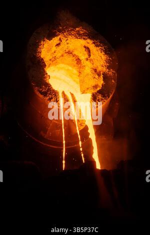 Metal casting process in metallurgical plant, molten metal is pouring from ladle, close up. Stock Photo