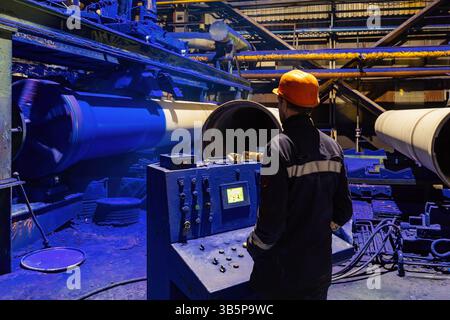 Factory engineer operates pipe painting automatic machine. Stock Photo