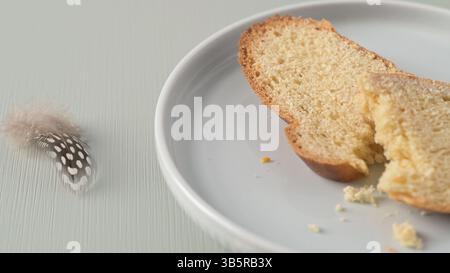 Folar slice with egg and feather on a white plate, a traditional Portuguese Easter bread. Stock Photo
