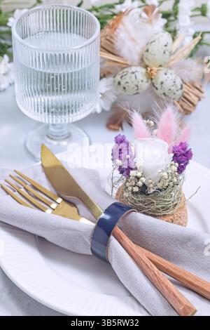 Festive easter table setting featuring elegant golden cutlery, a delicate floral centre piece, and subtle pastel decorations, vertical Stock Photo