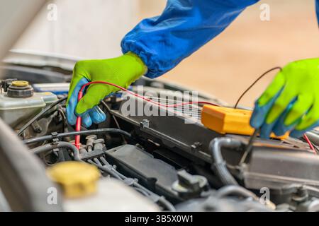 Electrical engineer uses multimeter to test electrical installation and motor current of a car in an auto workshop Stock Photo